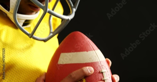 American football player holding ball against black background 