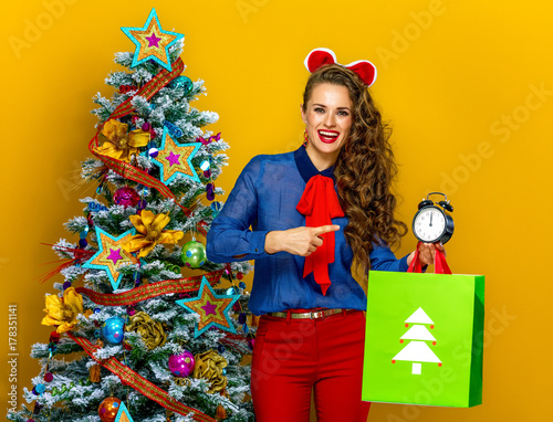 woman with Christmas shopping bag pointing at alarm clock