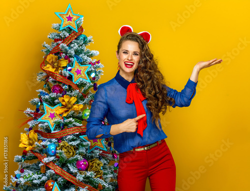 happy modern woman near Christmas tree pointing at empty palm
