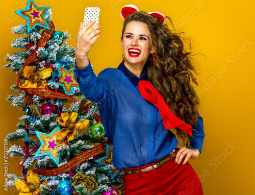 woman near Christmas tree with digital camera taking selfie