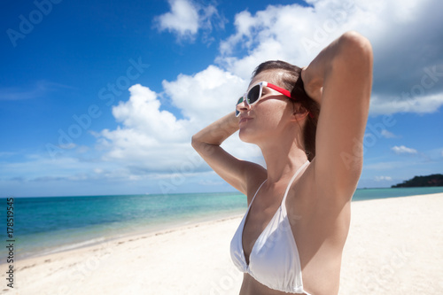 Beautiful young woman in a white bikini relaxes on the shore of a tropical island