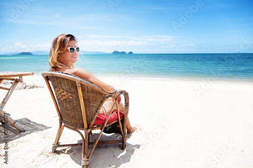 A beautiful young woman in a white bikini sits on a tropical beach. Rest, vacation, resort, beautiful life