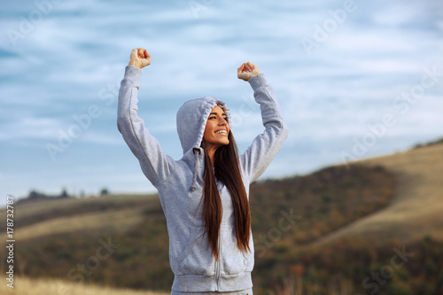 Young sport woman with raised arms motivates herself in nature