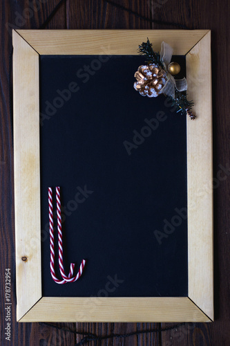 Wooden blackboard with place for your text with christmas candys and fir-cone.