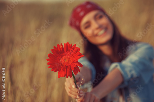 Beautiful young woman holding flower in a meadow. Focus on flower.