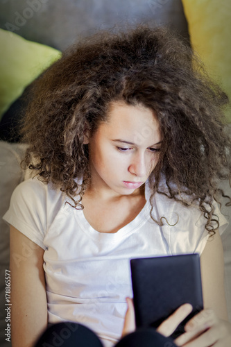 Teen girl resting and usiing digital tablet on sofa at home