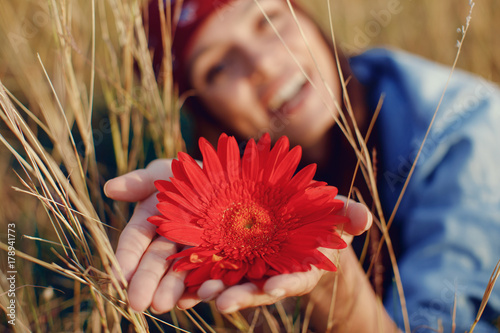 Beautiful young woman holding flower in a meadow. Focus on flower.
