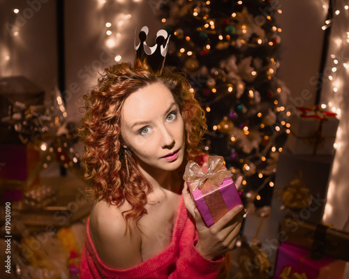portrait of beautiful young sexy curly red-haired girl on background merry christmas happy new year tree lights with star gift decor