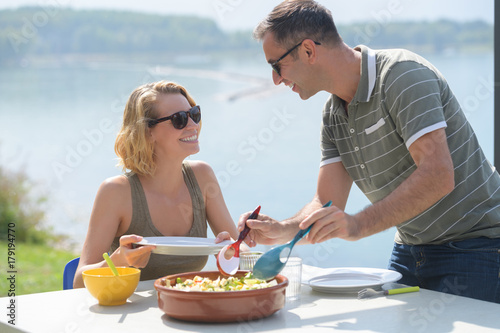 young couple eating a salad near a lake during summer