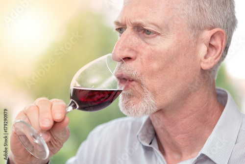 Mature man tasting red wine, light effect