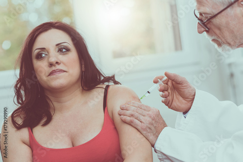 Doctor injecting vaccine to young woman, light effect