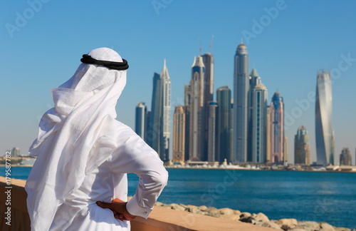 Plakat Nowoczesne budynki w Dubai Marina. Mężczyzna w arabskiej sukience patrzy na miasto
