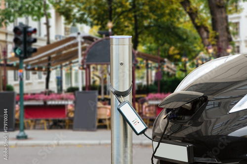 Zdjęcie XXL Samochód elektryczny jest ładowany na parkingu w pobliżu kawiarni ulicznej