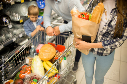 Plakat Wysokiego kąta portret szczęśliwa młoda rodzina z dziecko zakupy dla sklepów spożywczych w supermarkecie wpólnie, ono uśmiecha się podczas gdy pchający wózek na zakupy w nawie