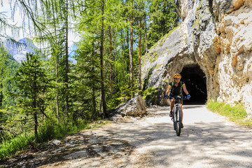 Tourist cycling in Cortina d'Ampezzo, stunning rocky mountains on the background. Family riding MTB enduro flow trail. South Tyrol province of Italy, Dolomites.