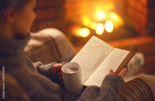 book and cup of coffee in hands of girl on  winter evening near fireplace © JenkoAtaman