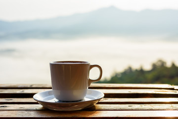 Close up white coffee cup on wood table and view of sunrise background