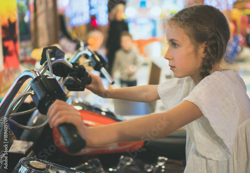 Zdjęcie XXL Mała dziewczynka bawić się motocykl symulator grę w parku tematycznym.