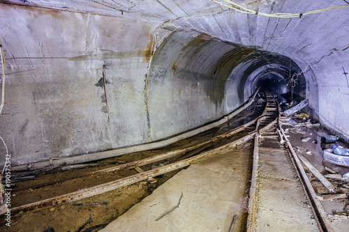 Plakat Bifurkacja zardzewiałej kolejki wąskotorowej. Tunel w opuszczonej kopalni. Obróć tunel. Światło z kolei.