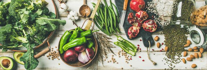 Winter vegetarian, vegan food cooking ingredients. Flat-lay of vegetables, fruit, beans, cereals, kitchen utencil, dried flowers, olive oil over white wooden background, top view. Clean eating food