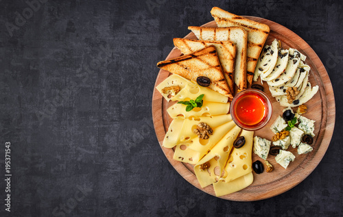 Plakat Płyta serowa: parmezan, cheddar, gouda, mozzarella i inne z bazylią na desce na ciemnym tle z miejscem na tekst. Miód i krakersy