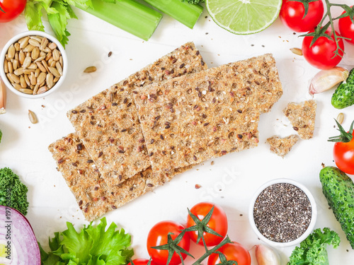 Zdjęcie XXL Odgórny widok całych zbożowych crispbreads żyto otaczał świeżych warzywa, zielenie i ziarna nad białym tłem ,. Pojęcie żywności ekologicznej i wegetariańskiej.