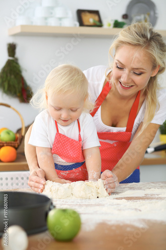Plakat Mała dziewczynka i jej blondynki mama w czerwonych fartuchach bawić się i śmia się podczas gdy ugniatający ciasto w kuchni. Domowe ciasta na chleb, pizzę lub upiecz ciasteczka
