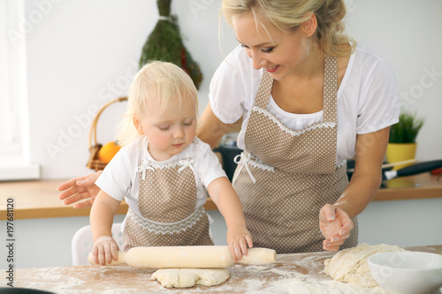 Plakat Mała dziewczynka i jej blondynki mama w czerwonych fartuchach bawić się i śmia się podczas gdy ugniatający ciasto w kuchni. Domowe ciasta na chleb, pizzę lub upiecz ciasteczka