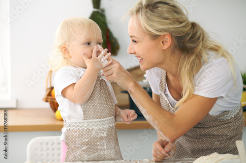Plakat Mała dziewczynka i jej blondynki mama w czerwonych fartuchach bawić się i śmia się podczas gdy ugniatający ciasto w kuchni. Domowe ciasta na chleb, pizzę lub upiecz ciasteczka