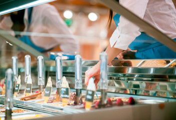 Confectioner serving ice cream from showcase fridge in pastry shop