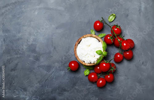 Plakat Miękki ricotta ser w drewnianej misce z zielonym basilem i czereśniowymi pomidorami, szarość kamienny tło, odgórny widok