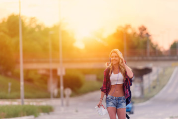 Beautiful young woman traveler with backpack walking along highway in sunset