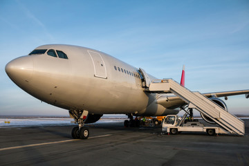 Wide body passenger airplane with boarding ramp at the winter airport apron