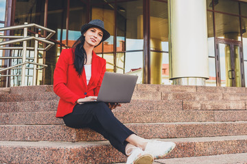 Happy hipster young woman working on laptop outdors. Student girl using laptop in university campus. Toned image.
