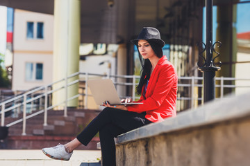 Happy hipster young woman working on laptop outdors. Student girl using laptop in university campus. Toned image.