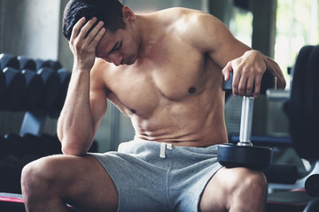 Fitness man with dumbbell tired and resting in gym