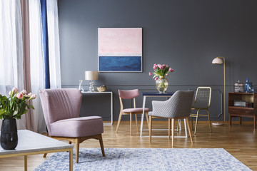 Pink armchair in spacious grey dining room interior with flowers on table and painting on the wall