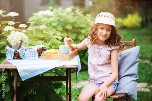Фото: happy child girl drinking tea with lemons in summer garden in the morning. happy child girl drinking tea with lemons in summer garden in the morning.