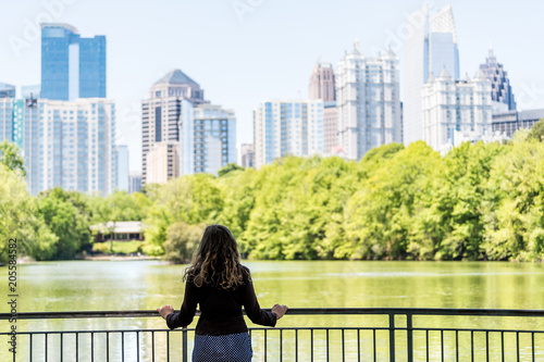 Plakat Młoda kobieta stoi w Piedmont Park w Atlancie, Georgia patrząc na malownicze wody i panoramę miasta miejskich drapaczy chmur w centrum, Lake Clara Meer