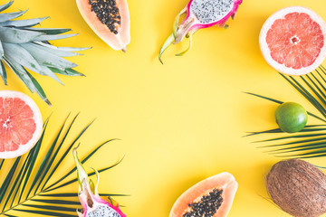 Summer fruits. Tropical palm leaves, pineapple, coconut, papaya, dragon fruit, orange on yellow background. Summer concept. Flat lay, top view, copy space