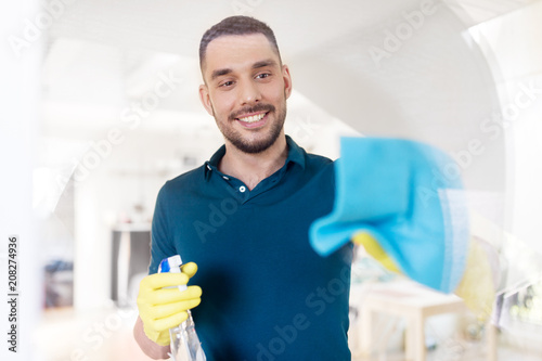 Фото: household and people concept - man in rubber gloves cleaning window with rag and spray cleaner at home household and people concept - man in rubber gloves cleaning window with rag and spray cleaner at home