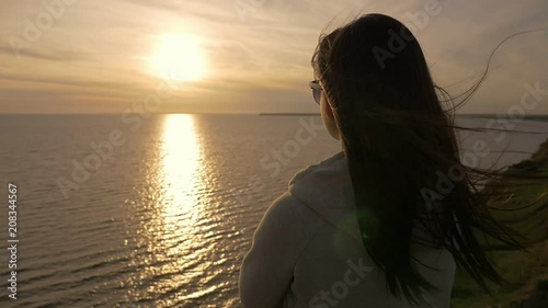 Видео: Back view of a romantic girl with long loose hair in a white suit standing on the Black Sea beach and looking at sparkling sunset in summer Back view of a romantic girl with long loose hair in a white suit standing on the Black Sea beach and looking at sparkling sunset in summer