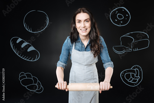 Фото: Professional cook. Kind professional cook feeling happy and smiling while using a wooden rolling pin Professional cook. Kind professional cook feeling happy and smiling while using a wooden rolling pin