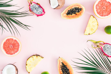 Summer fruits. Tropical palm leaves, pineapple, coconut, papaya, dragon fruit, orange on pastel pink background. Flat lay, top view, copy space