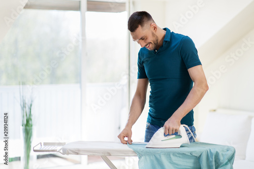 Фото: housework and household concept - man ironing shirt on iron board at home housework and household concept - man ironing shirt on iron board at home