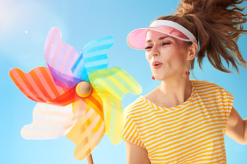 happy fit woman against blue sky blowing on colorful windmill