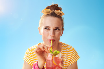 smiling woman against blue sky drinking refreshing cocktail