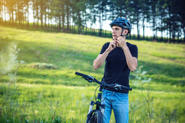 Cyclist is wearing a sports helmet on his head in the background of green nature. Concept of protection during Cycling