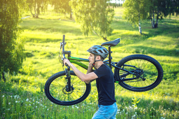 Cyclist man in helmet carries his mountain bike in the rise in the background green nature. Active and healthy lifestyle