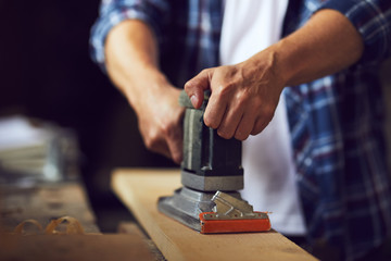 Carpenter working in his workshop with electric sander on wooden board